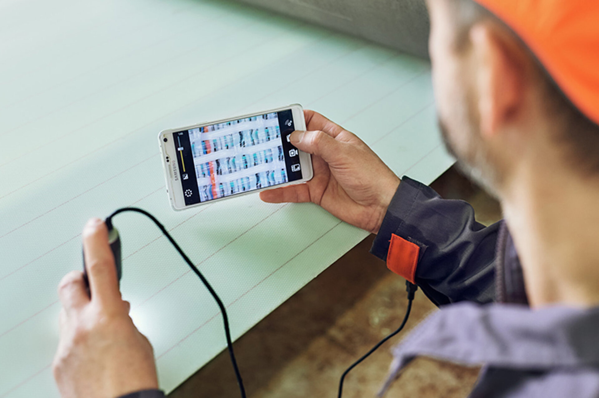 Ein Mitarbeiter des technischen Services von Heimbach nimmt mittels Licht und mithilfe einer Smartphone-App eine optische, berührungslose Nasssiebmessung an der Papiermaschine vor.