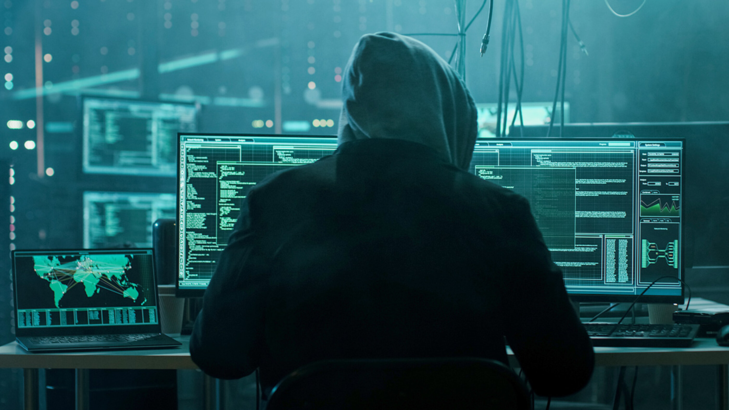 Ein Cyberkrimineller startet einen Cyberangriff auf T-Systems / Deutsche Telekom. Ein Cyberkrimineller in sitzt in einem dunklen Raum und startet einen Cyberangriff auf das Unternehmen T-Systems / Deutsche Telekom.
