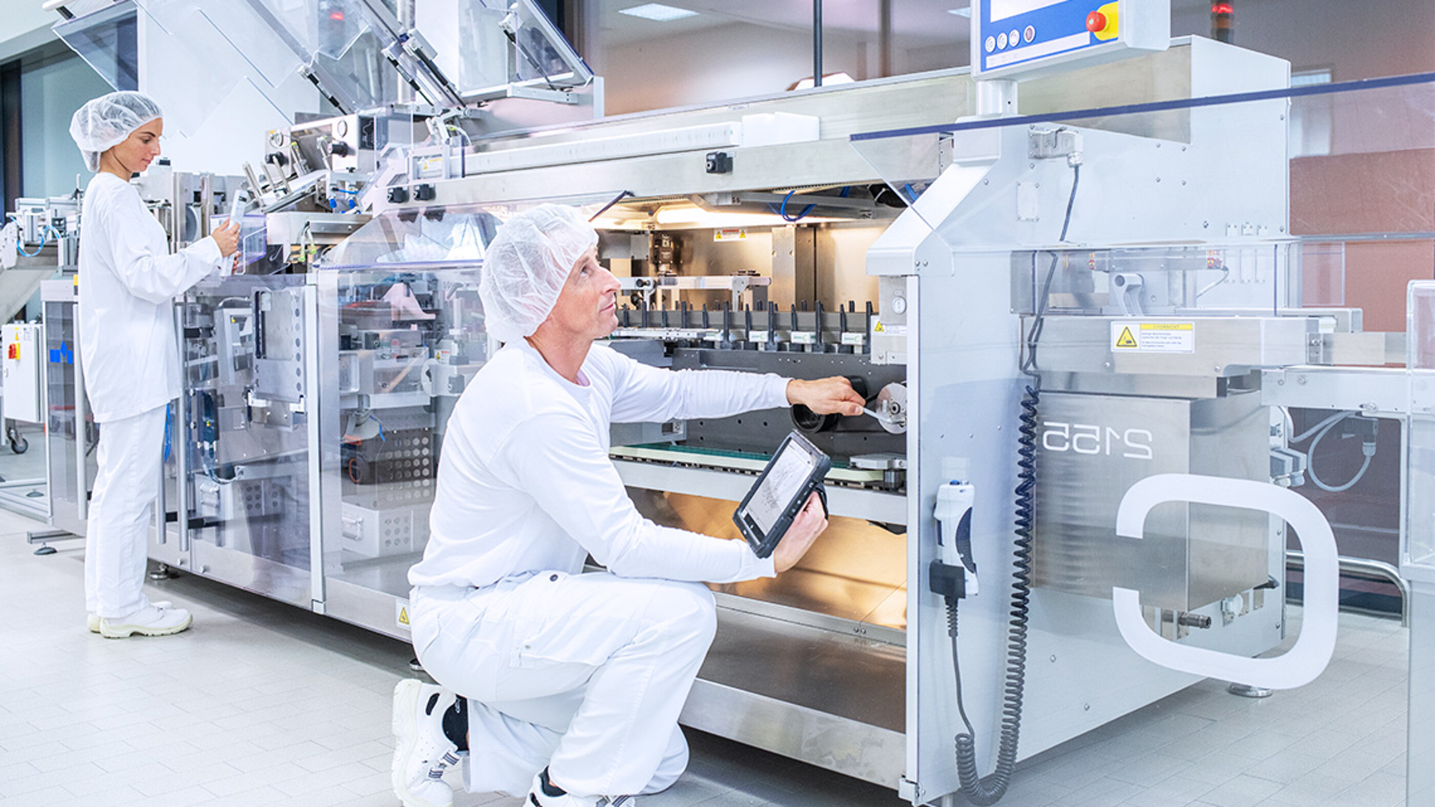 Die Marken-Bildwelt stellt die moderne Pharma-Konfektionierung dar, in der Pastillen als Bulkware, in Blisterstreifen und Fertigpackungen verpackt werden. Die BOLDER Arzneimittel Bildwelt zeigt zwei Mitarbeiter, die an einer Anlage zur Verpackung der Pastillen arbeiten.