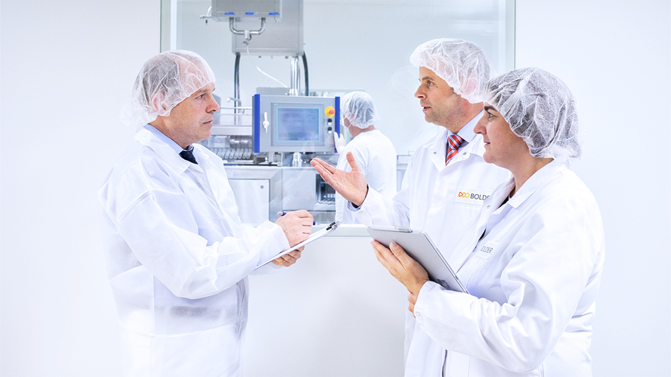 Die Marken-Bildwelt schafft Vertrauen und zeigt ein Audit in der Produkt-Herstellung. Die BOLDER Arzneimittel Bildwelt zeigt Verantwortliche Personen, die in der Pastillen Produktion mit einem Auditor sprechen.