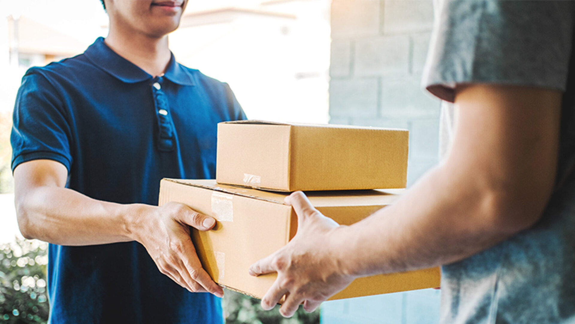 Steigender Online-Handel führt zu einer höheren Nachfrage nach Verpackungspapieren. Der Bote eines Lieferdienstes übergibt an der Haustür zwei Pakete an den Empfänger.